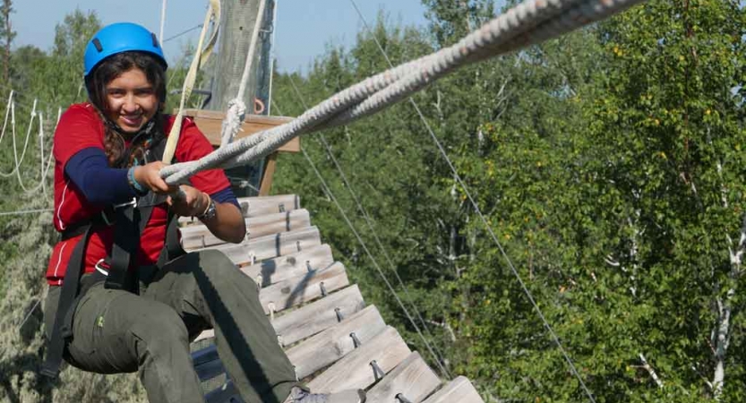 a students holds onto a rope while completing a ropes course with outward bound